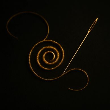 alt="Golden thread forms a protective spiral knot around a small ring, a needle paused mid-stitch."