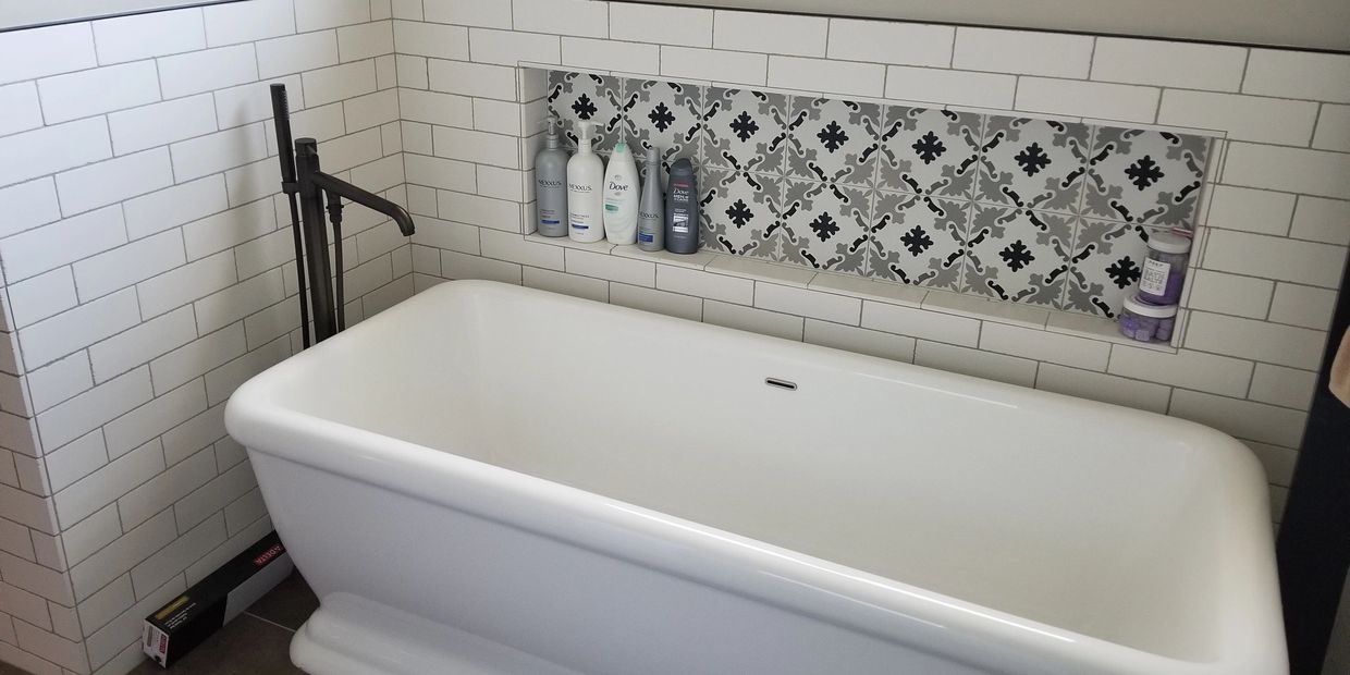 White bathtub with tiled wall and bathroom products on shelf.