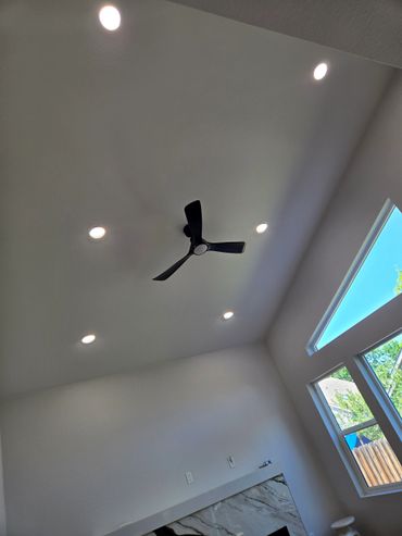 Modern ceiling with black fan, recessed lights, and large windows.