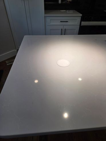 A clean white kitchen countertop with reflections of overhead lights.