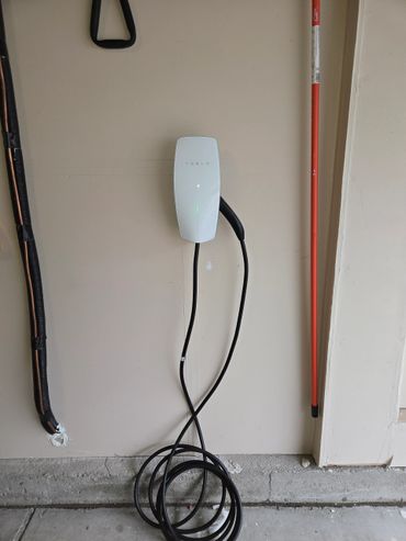 Tesla electric vehicle charger mounted on a garage wall with coiled cable.