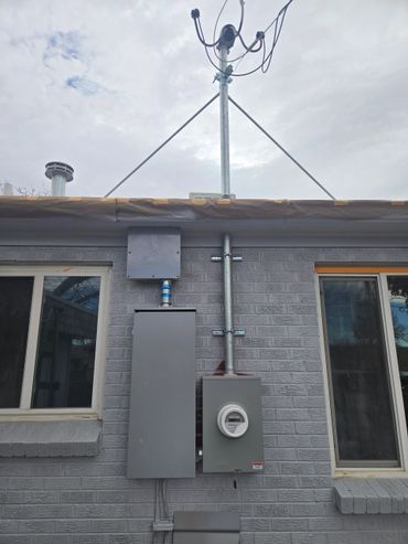 Electrical meter and panel installed on a gray brick wall between two windows.