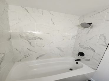 Modern white bathtub with marble tile walls and black fixtures.