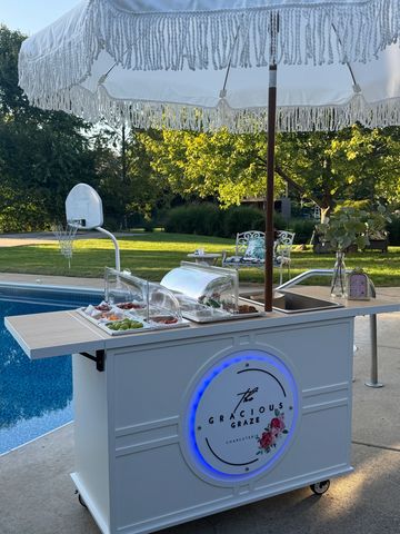 Elegant outdoor snack cart by the pool with umbrella.