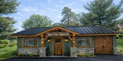 A charming green building with wooden accents labeled Spa City Speech.