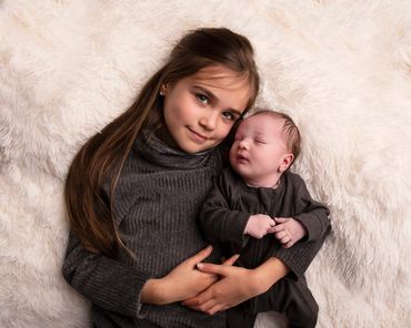 award winning image of a young girl holding her newborn brother on a fur rug