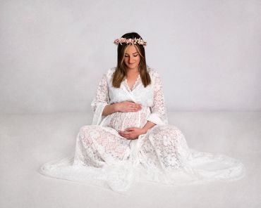 pregnant lady dressed in white with pink flower crown looking down at her baby bump
