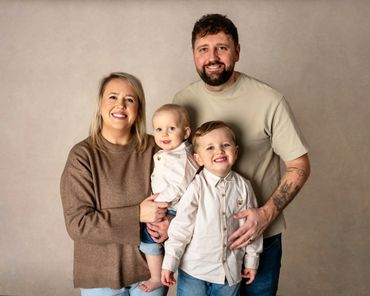 Smiling family of four posing together against a neutral backdrop.