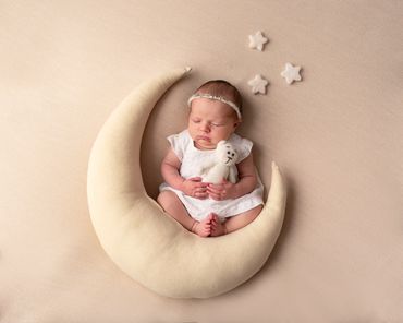 sleeping baby girl in a crescent moon with stars and holding a white knitted teddy