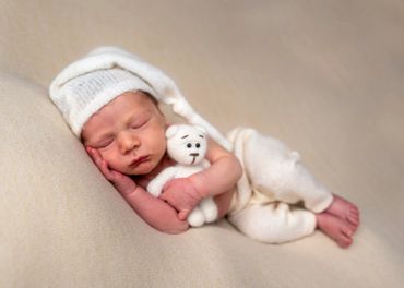 sleeping newborn lay on his side holding a teddy bear and wearing a sleeping cap
