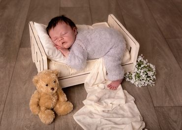 newborn sleeping on a bed with teddy bear