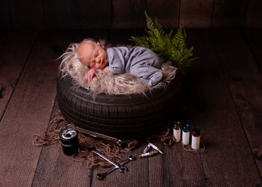newborn boy asleep in fur on a car tyre with mechanics tools