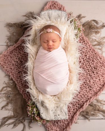 newborn girl swaddle in pink in a trench bowl filled with fur on prink chunky knit blanket