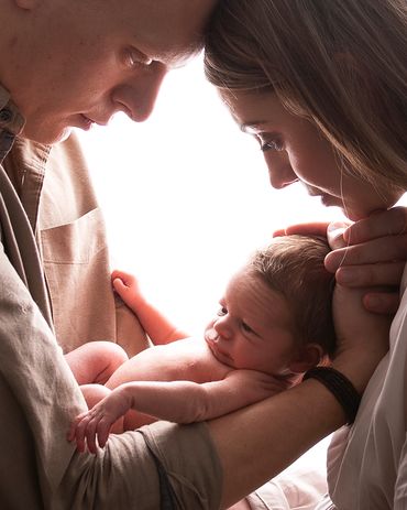 backlit image of parents looking down on their newborn
