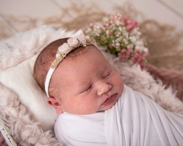 newborn girl asleep, wrapped in white with a white headband