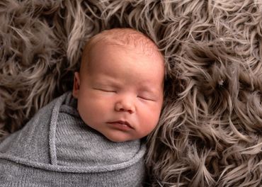 newborn baby sleeping, swaddled in grey on brown fur