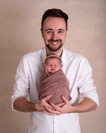 proud father holding his newborn baby girl who is asleep and swaddled in pink with matching headband