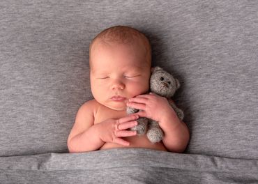 sleeping baby boy cuddling a grey knitted teddy bear
