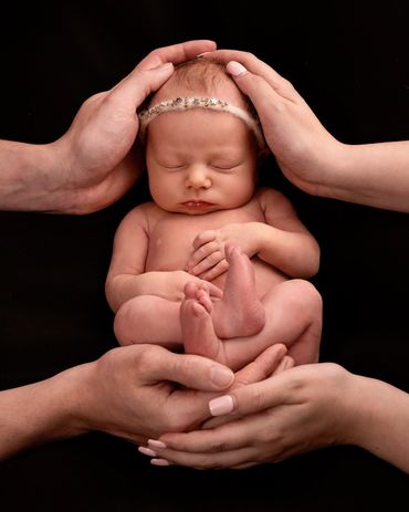 sleeping baby girl in a stars headband supported by her parents hands