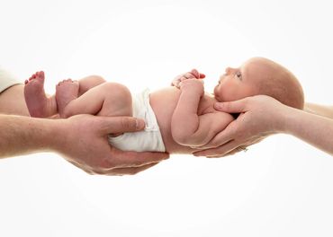 newborn baby suspended by mum and dads hands