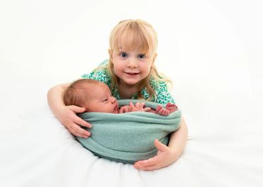 excited big sister holding newborn baby