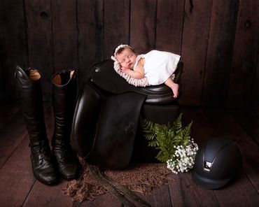 sleeping baby girl on a saddle with riding boots and helmet