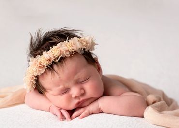 chubby cheeked newborn wearing a peach flower head band, asleep