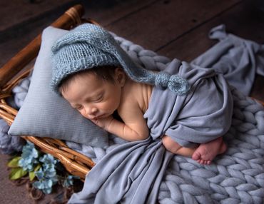 tiny newborn boy asleep in a basket on top of a chunky blue woolen blanket