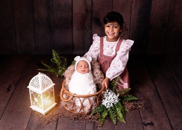 happy older sister with newborn brother in a basket with a lantern