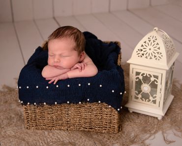 newborn baby asleep in a basket next to a lantern on a white wood floor
