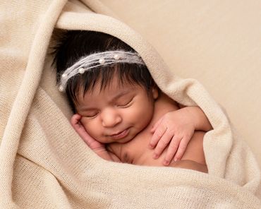 sleeping newborn girl in a pearl headband peeping out of a cream knitted blanket