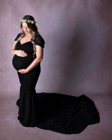 pregnant lady in black gown and flower crown, holding and looking down at her pregnancy bump