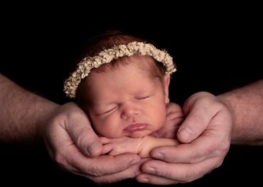 sleeping baby girl waring a dried flower headband supported in her fathers hands