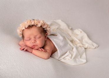 newborn girl asleep with her chin on her hands wearing a preach flower halo