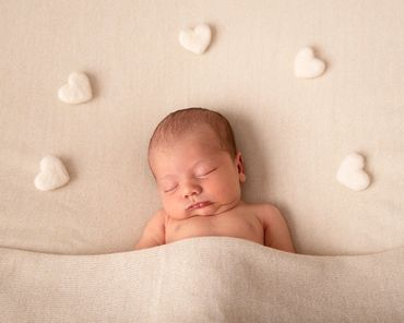 newborn asleep on cream background surrounded with white felted hearts