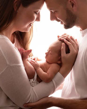 backlit image of parents looking down on their newborn baby