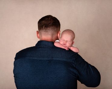 Father facing away with baby resting on his shoulder asleep