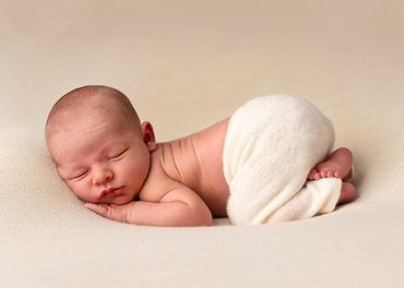 newborn asleep in tushie up pose wearing cream pants