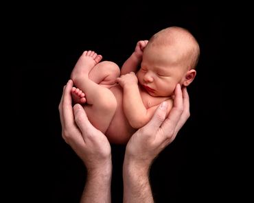 sleeping newborn held in the air by dads hands
