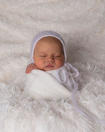 newborn swaddled in a white knitted wrap in a white woolen hat on white fur
