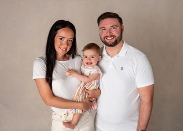 A happy family portrait with parents and their baby smiling.