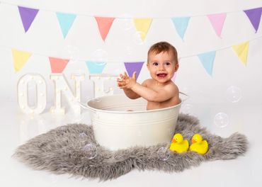 Happy baby playing in a tub with colorful decorations and rubber ducks.