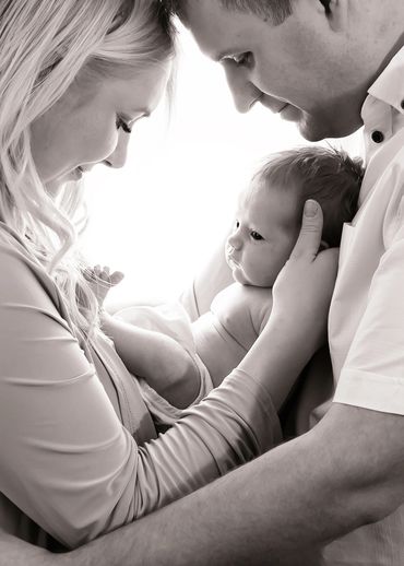 black and white image of loving parents gazing down on their wide eyed newborn