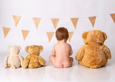 A baby sitting with three teddy bears in front of decorative flags.