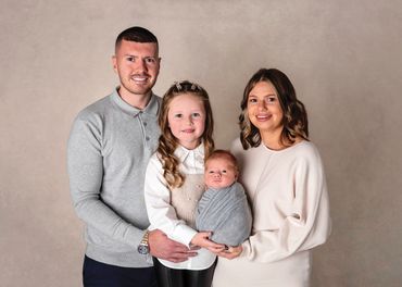 Parents and older sibling holding wide eyed newborn boy who is swaddled in grey
