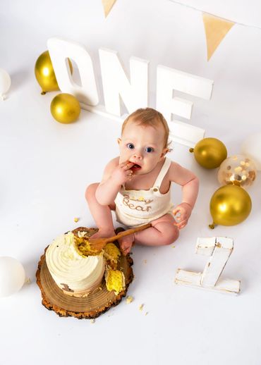 Baby enjoying first birthday cake with gold and white decorations.