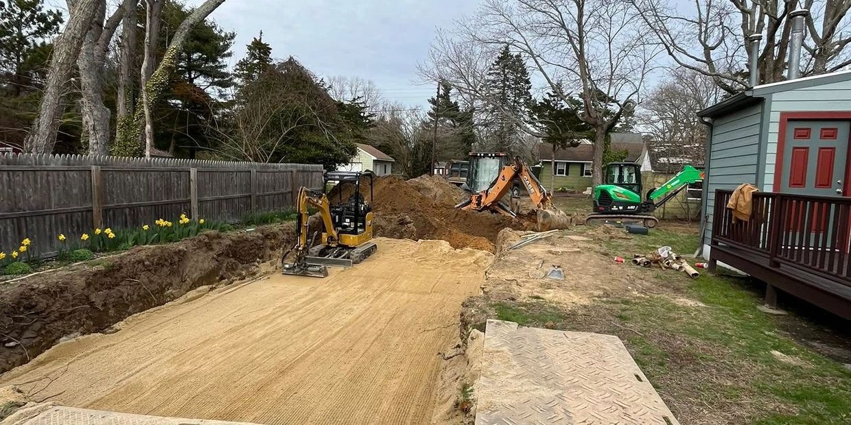 Construction site with excavators digging a large trench beside a house.