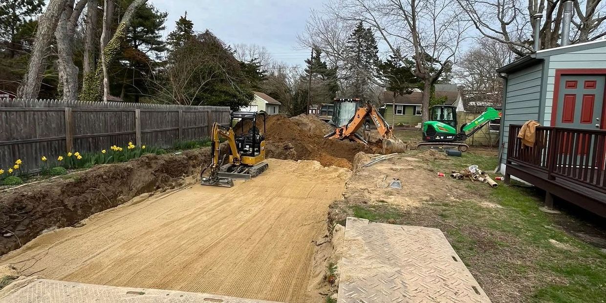 Construction site with excavators digging a large trench beside a house.