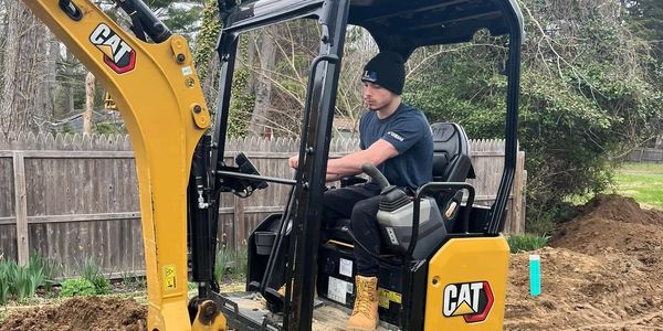 Person operating a CAT mini excavator in a dirt area.