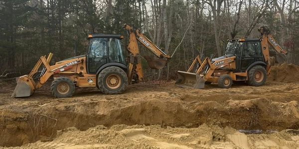 Two CASE backhoe loaders parked on a construction site surrounded by trees.